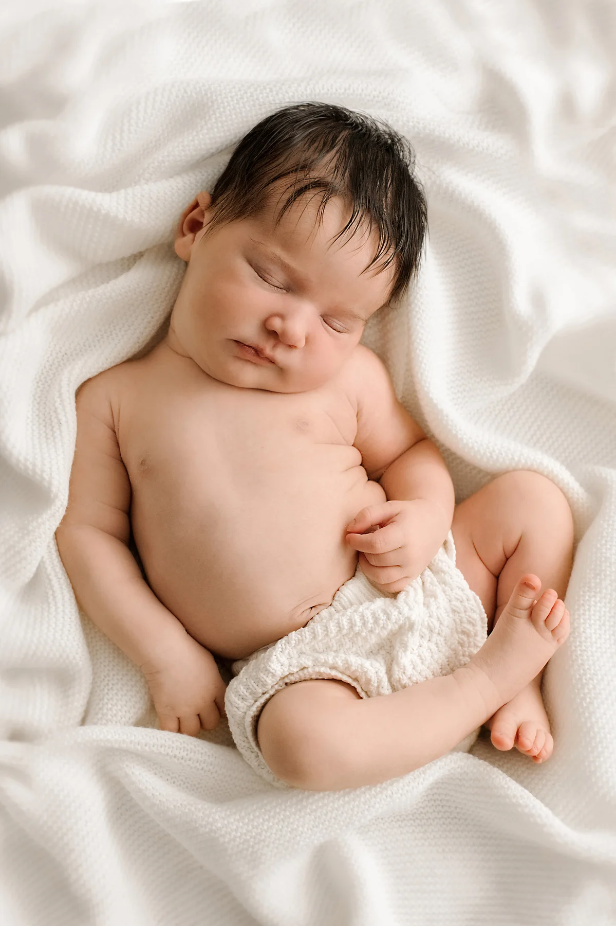 A sleeping newborn resting peacefully on soft white linen